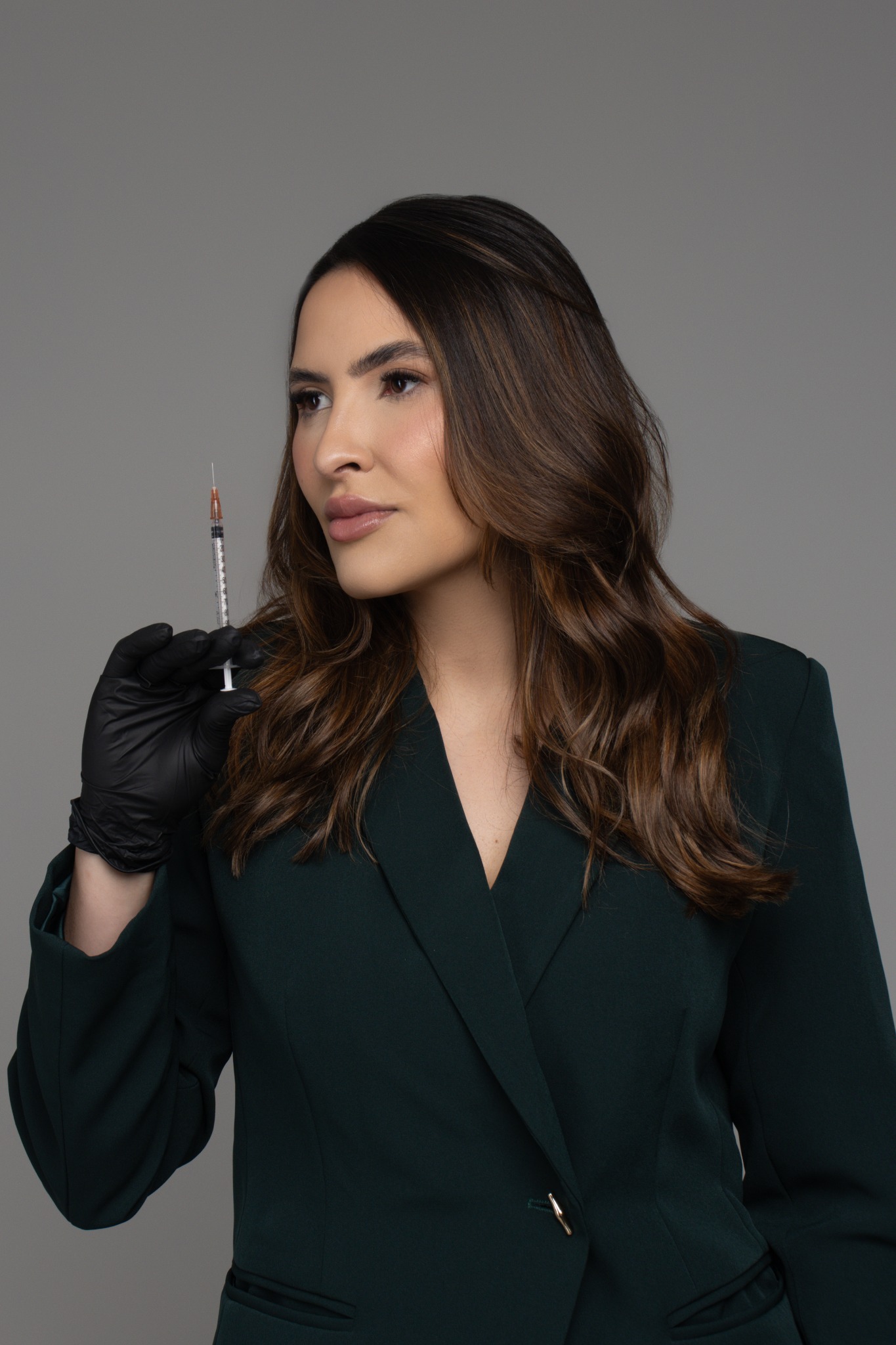 Dra. Kathellyn Moreira usando blazer verde escuro e segurando uma seringa